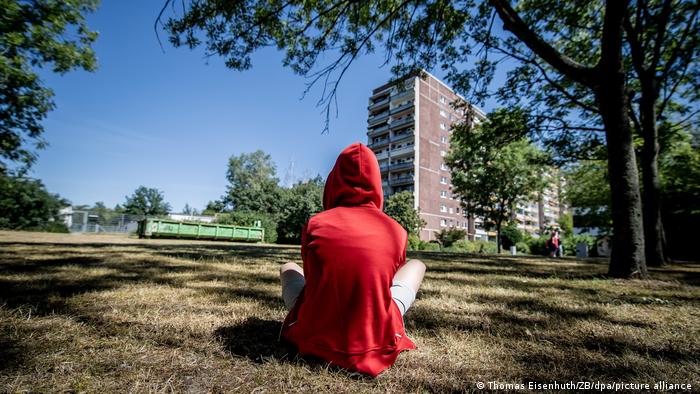 A young person wearing a hoodie sitting on grass with their back to the camera