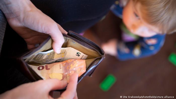 Ein Kind schaut zu, während ein Erwachsener seine Geldbörse öffnet und fünfzehn Euro findet