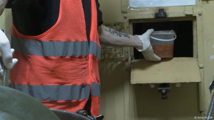 A man in an orange vest pushing food through a hatch