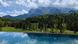 A photo of a pool with a view to the alps and a green forest. A photo of a pool with a view to the alps and a green forest.