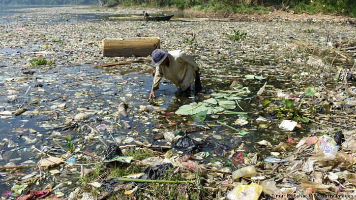 A man stands in a river full of plastic 