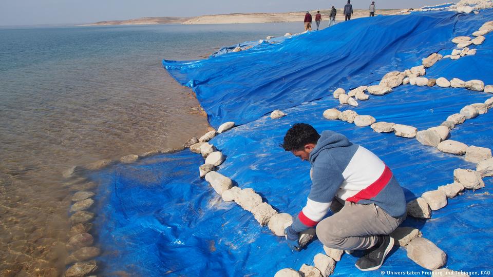 Homem cobra ruínas arqueológicas com plástico azul e pedras