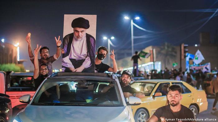 A car with a poster of Moqtada al-Sadr on the roof, people waving from inside