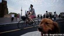 A man wearing a protective face mask cycles past people and a dog on a bridge, as the city prepares to end the lockdown placed to curb the coronavirus disease (COVID-19) outbreak in Shanghai, China May 31, 2022. REUTERS/Aly Song