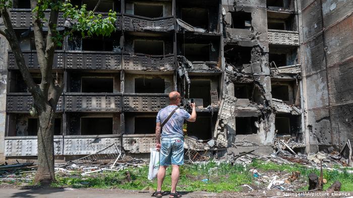A man stands in front of a heavily damaged building in Kharkiv, Ukraine