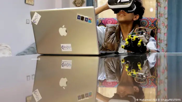 A teenager is seen wearing virtual reality devices on his eyes and left hand as he works from home