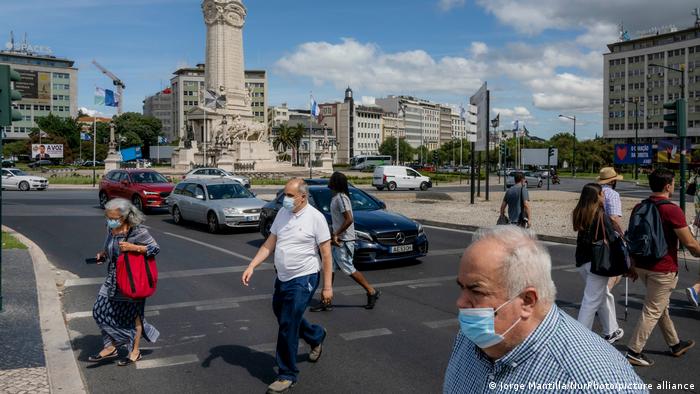 People are seen wearing masks walking near the monument to the Marquis of Pombal in Lisbon, Portugal