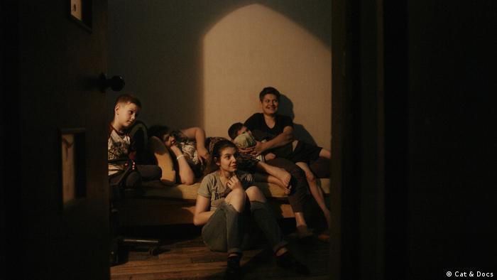 In einer Szene des Films The Earth is Blue as an Orange sitzen vier Kinder und ihre Mutter lächelnd auf einer Couch.