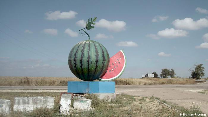 Photo from the film 'Volcano': sculpture of a giant watermelon at the corner of the road between the fields.