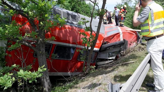 Emergency workers walk along a derailed train carriage that has crashed into trees