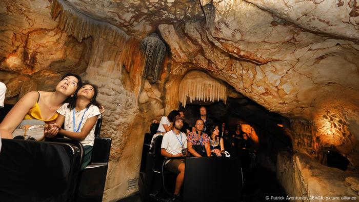 Menschen sitzen in kleinen Waggons und fahren durch den Nachbau der Cosquer-Höhle in Marseille. 
