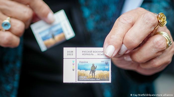 Claudia Roth holds up a stamp showing a Ukrainian soldier gesturing to Russia's Black Sea fleet