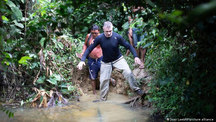 British journalist Dom Phillips (r) seen wading through muddy waters followed by a Yanomami Indigenous man (l)