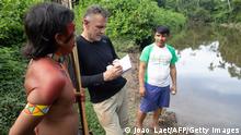Veteran foreign correspondent Dom Phillips (C) talks to two indigenous men in Aldeia Maloca Papiú, Roraima State, Brazil, on November 16, 2019. - Phillips went missing while researching a book in the Brazilian Amazon's Javari Valley with respected indigenous expert Bruno Pereira. Pereira, an expert at Brazil's indigenous affairs agency, FUNAI, with deep knowledge of the region, has regularly received threats from loggers and miners trying to invade isolated indigenous groups' land. (Photo by Joao LAET / AFP) (Photo by JOAO LAET/AFP via Getty Images)