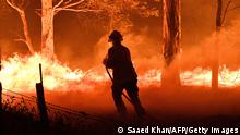 TOPSHOT - This picture taken on December 31, 2019 shows a firefighter hosing down trees and flying embers in an effort to secure nearby houses from bushfires near the town of Nowra in the Australian state of New South Wales. - Fire-ravaged Australia has launched a major operation to reach thousands of people stranded in seaside towns after deadly bushfires ripped through popular tourist areas on New Year's Eve. (Photo by SAEED KHAN / AFP) (Photo by SAEED KHAN/AFP via Getty Images)