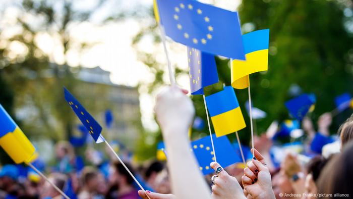Menschen halten Fahnen der Ukraine und EU in ihren Händen