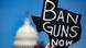 Com Capitólio ao fundo, mão segura cartaz com dizer: Banimento de armas agora Com Capitólio ao fundo, mão segura cartaz com dizer: Banimento de armas agora