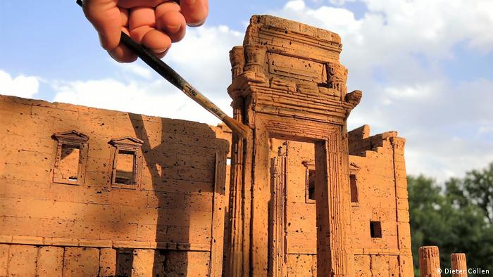 Die Hand eines Mitarbeiters führt mit einem Pinsel letzte Arbeiten an einem Korkmodell des Baal-Tempels von Palmyra aus, der 2015 vom sogenannten IS zerstört wurde.