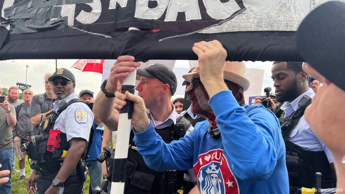 A man holding a pro-gun placard is led away from the protest by police