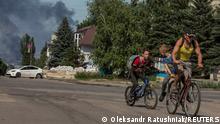 10.06.2022***A local man with kids rides a bicycle along an empty street, as smoke rises after shelling in the background, amid Russia's attack on Ukraine, in the town of Lysychansk, Luhansk region, Ukraine June 10, 2022. Picture taken June 10, 2022. REUTERS/Oleksandr Ratushniak TPX IMAGES OF THE DAY