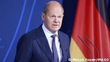 German Chancellor Olaf Scholz speaks in front of a German flag