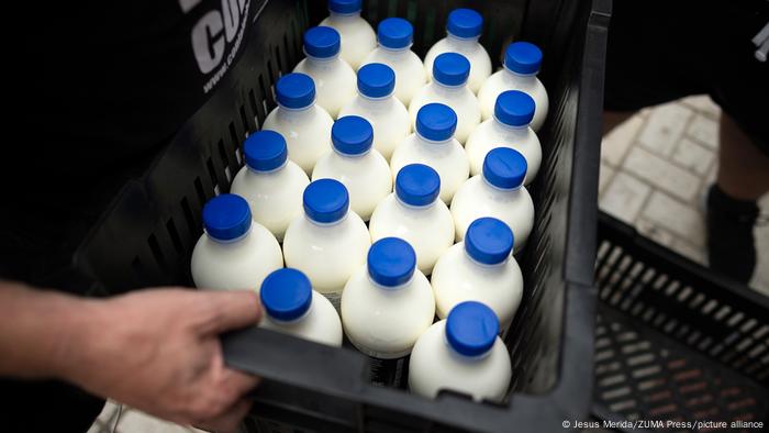 Hombre sujeta un cesto de plástico negro con botellas de leche.