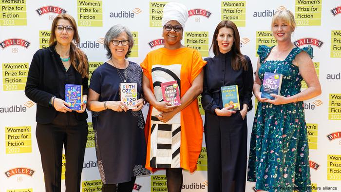 Elif Shafak, Ruth Ozeki, Lisa Allen-Agostini, Meg Mason and Maggie Shipstead stand left to right in front of a backdrop while holding their novels