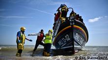 TOPSHOT - Royal National Lifeboat Institution's (RNLI) members of staff help migrants to disembark from one of their lifeboat after they were picked up at sea while attempting to cross the English Channel, on the beach of Dungeness, on the southeast coast of England, on June 15, 2022. - Furious Conservatives called on Britain's government on June 15, 2022 to abandon a European human rights pact after a judge dramatically blocked its plan to fly asylum-seekers to Rwanda. Under the UK's agreement with Rwanda, all migrants arriving illegally in Britain are liable to be sent to the East African nation thousands of miles away for processing and settlement. The government, after arguing that Brexit would lead to tighter borders, says the plan is needed to deter record numbers of migrants from making the perilous Channel crossing from northern France. (Photo by Ben Stansall / AFP)