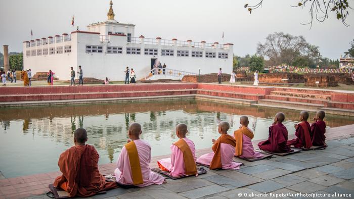 Buddhisten sitzen am Rande eines Wasserbeckens vor dem Maja Devi Tempel in Lumbini, Nepal
