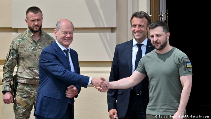 Olaf Scholz gibt dem ukrainischen Präsidenten Wolodymyr Selenskyj die Hand, dahinter Emmanuel Macron