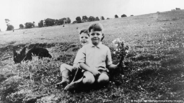 Black-and-white photo of Paul McCartney at the age of 6, holding flowers with his eight-year-old brother Mike, 