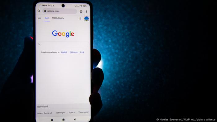 Hand is holding a smartphone with the Google logo displayed and dark blue background