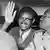 A picture of Patrice Lumumba waving from his car, in black and white