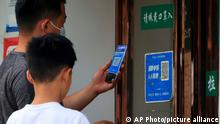 A man wearing a face mask scans a QR code for a health monitoring app to enter a shop in Zhengzhou in central China's Henan Province, Friday, June 17, 2022. Angry bank customers who traveled to a city in central China attempting to retrieve their savings from troubled rural banks were stopped in their tracks by a common technology: a QR code. (Chinatopix via AP)