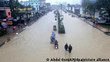 18.06.2022, Bangladesch, Sylhet: Menschen waten durch eine überschwemmte Straße. Mehrere Menschen sind bei Überschwemmungen im Nordosten Indiens und in Bangladesch ums Leben gekommen, Millionen von Häusern stehen unter Wasser. Beide Länder haben das Militär um Hilfe bei der Bekämpfung der schweren Überschwemmungen gebeten, die sich noch verschlimmern könnten, da für das Wochenende weitere Regenfälle erwartet werden. Foto: Abdul Goni/AP/dpa +++ dpa-Bildfunk +++