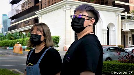 Two people wearing black face masks stand on a busy street in Taiwan