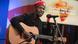 Bobi Wine in black shirt and red hat singing and playing the guitar