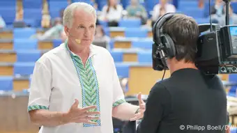 Timothy Snyder in a white dress shirt with blue-green applications talking into the camera