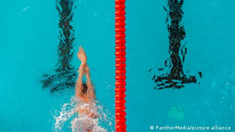 A person swims in a pool as seen from above, next to a red dividing lane