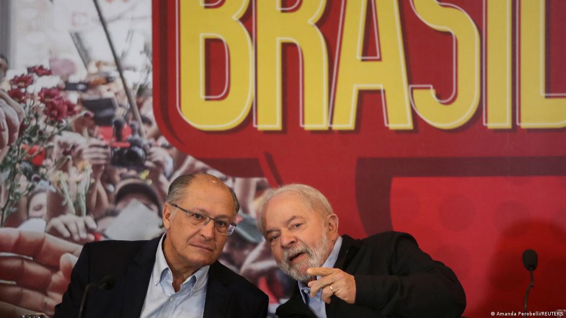 Alckmin e Lula conversam em frente a faixa onde está escrito Brasil