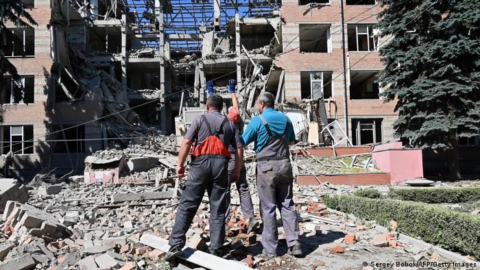 Workers stand outside a partially destroyed building in Kharkiv which was targeted by a rocket attack