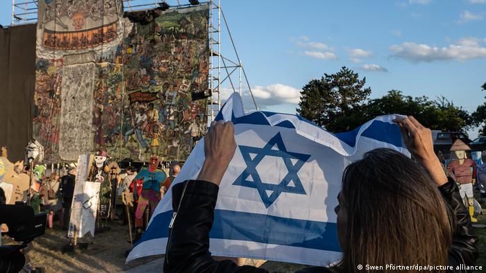 Abbau des Bildes People's Justice, davor hält eine Frau eine Israel-Flagge hoch. 