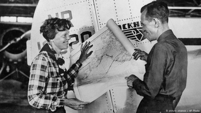 Amelia Earhart und Navigator Fred Noonan lachen über einer ausgebreiteten Karte.