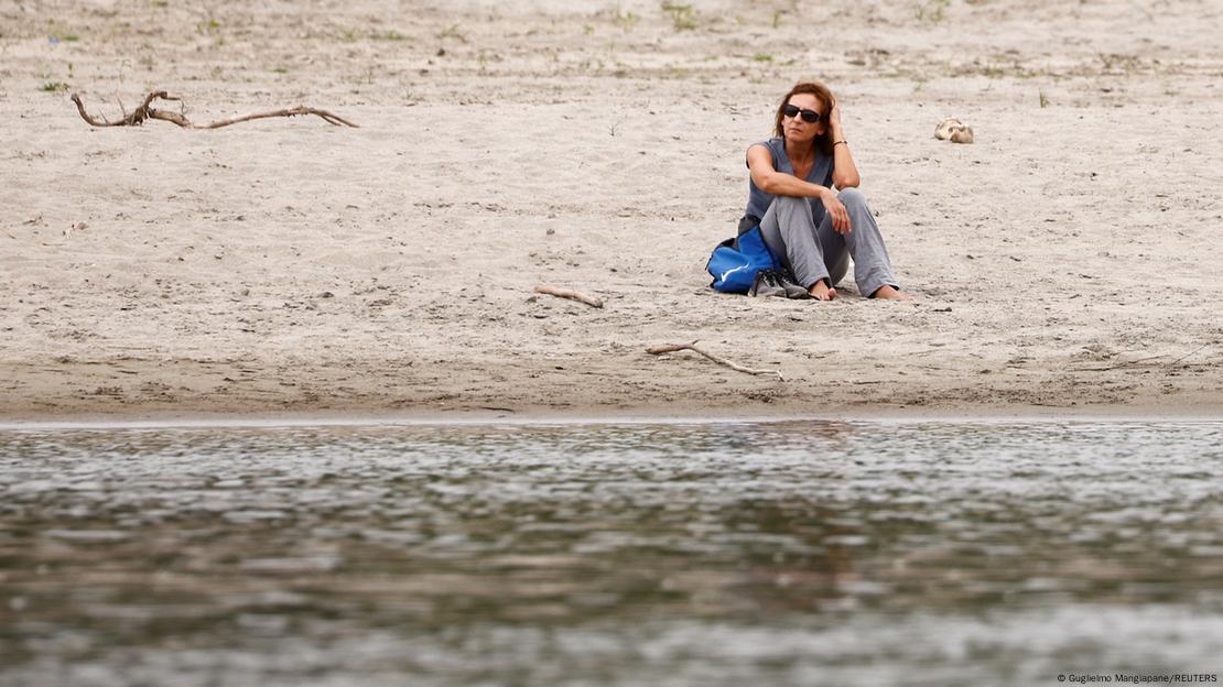 Mulher sentada à beira de um rio com pouca água