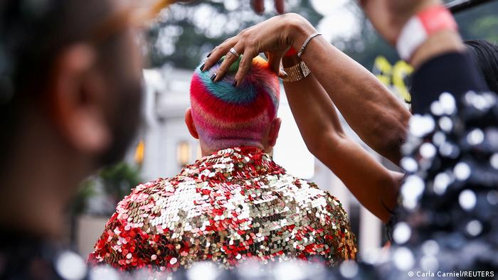 A person rubs the head of another parade participant in Sao Paulo; the person's hair is dyed in rainbow colors