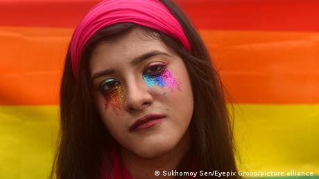 An activist in Calcutta wearing face paint, in front of a rainbow flag