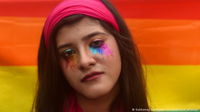 An activist in Calcutta wearing face paint, in front of a rainbow flag