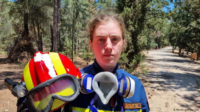 Volunteer firefighter Katerina Kaglia, with helmet and respirator, stands at a fork in the road in the woods outside Vyronas, Greece