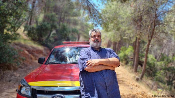 Stavros Salayiannis stands in front of his red Ford pick-up on a fire trail in the woods near Vyronas, Greece