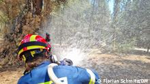 A firefighter with a hose over her shoulder sprays water into the forest in Vyronas, Greece